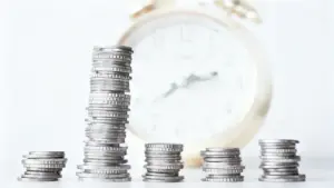 Pile di monete davanti a una sveglia sfocata, concetto di tempo e denaro