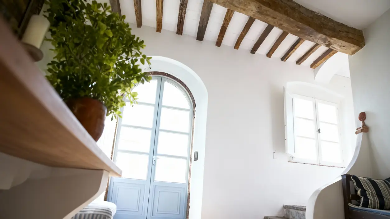 Ingresso luminoso con porta in legno chiaro, soffitto con travi a vista e dettagli decorativi
