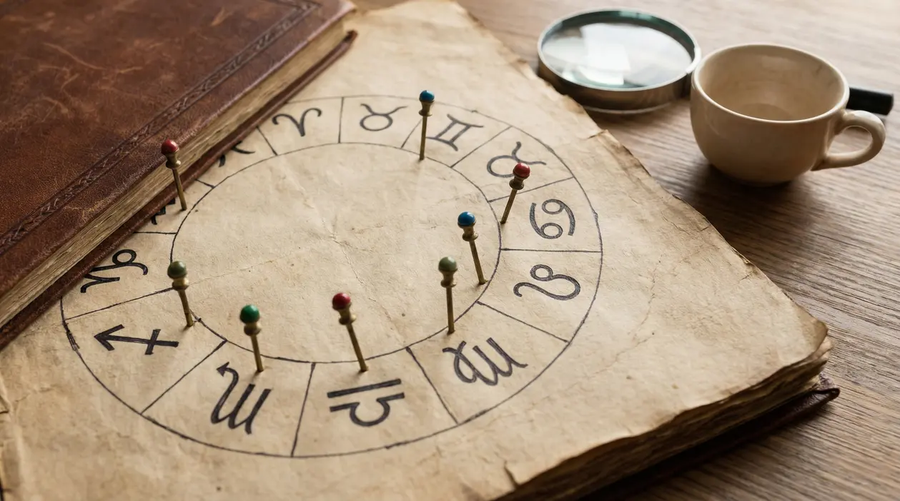 Vecchio libro con cerchio zodiacale e puntine colorate su simboli astrologici