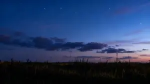 Cielo notturno stellato sopra un campo all'imbrunire con alcune nuvole